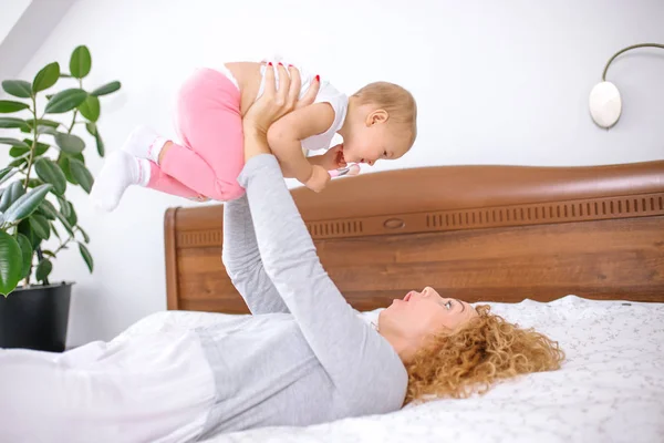 Happy awesome ginger woman raising her baby while lying on the bed — Stock Photo, Image