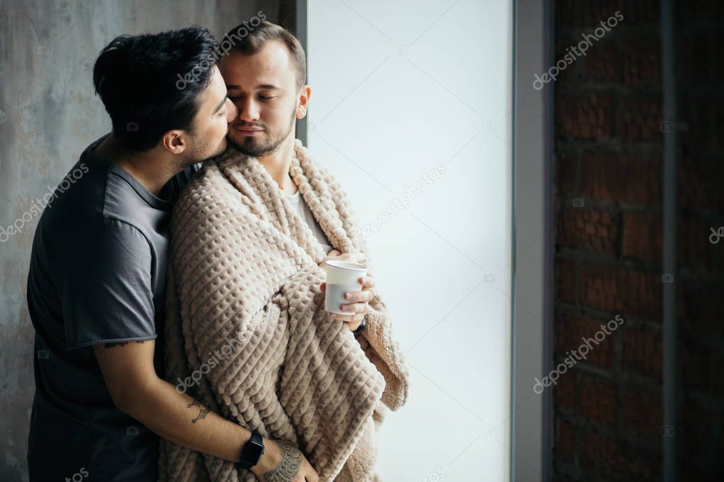 two handsome homosexual guys while standing near window