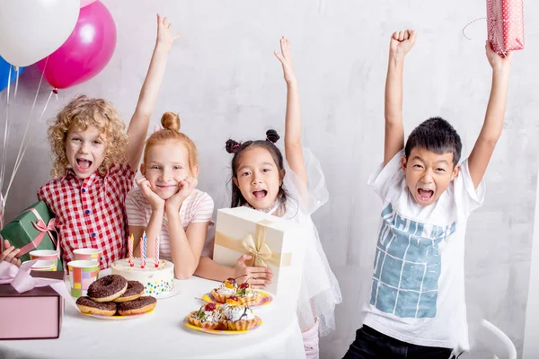 Crianças felizes levantando as mãos juntas na festa de aniversário — Fotografia de Stock