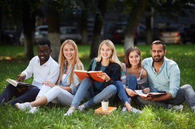 Karışık ırk grup birlikte üniversite kampüsü yeşil çimenlerin üzerine oturmuş öğrenci