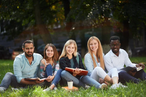 Grupo mixto de estudiantes sentados juntos en el césped verde del campus universitario — Foto de Stock