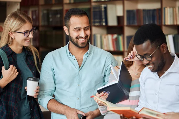 Retrato de jovens amigos multiculturais lendo livros juntos na biblioteca — Fotografia de Stock