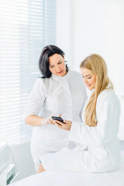 Kvinna med kosmetolog får tid för nästa besök, använder smartphone i salong — Stockfoto