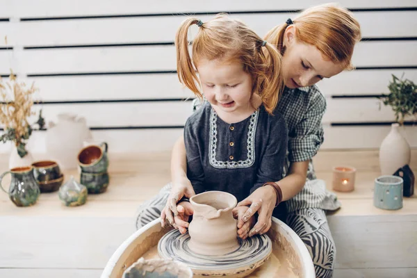 Chica pelirroja enseñando a su hermana pequeña a crear un jarrón de arcilla —  Fotos de Stock