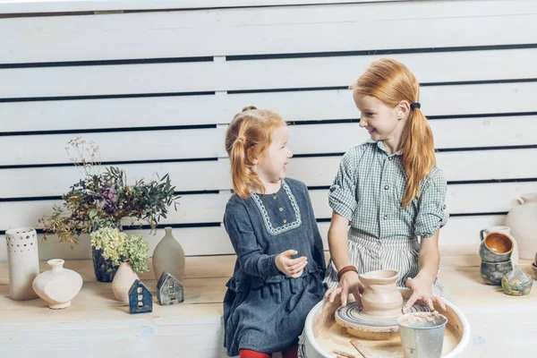 Niñas pequeñas y encantadoras hablando entre sí mientras hacen jarra en la rueda de cerámica —  Fotos de Stock