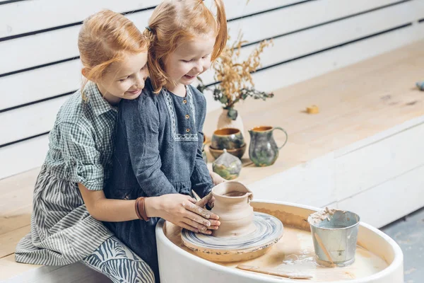 Chica dando una mano a su pequeña hermana agradable para esculpir la olla — Foto de Stock