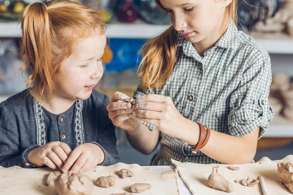 Chica mostrando su hermana pequeña para crear una arcilla juguetes — Foto de Stock