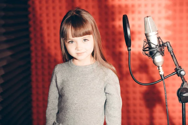 Vacker liten flicka med mikrofon på röd bakgrund — Stockfoto