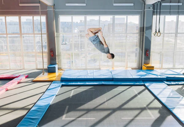 Junger fitter, flexibler Kerl beim komplexen Salto auf dem Trampolin — Stockfoto