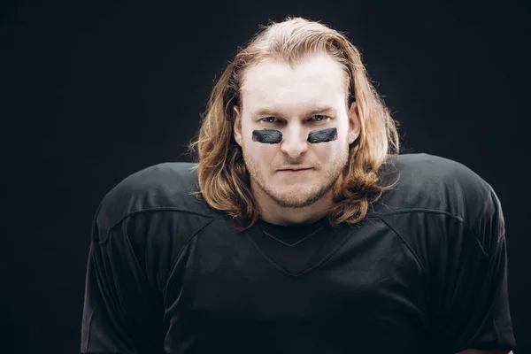 Determined American football player posing with painted face and chewing gum