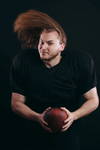Confident american football player in black sportwear holding helmet and ball