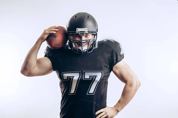 Musculoso futbolista americano en uniforme protector y casco sosteniendo pelota — Foto de Stock