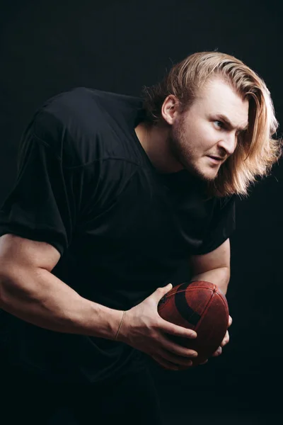 Entschlossener American-Football-Spieler in Aktion isoliert auf schwarzem Hintergrund — Stockfoto