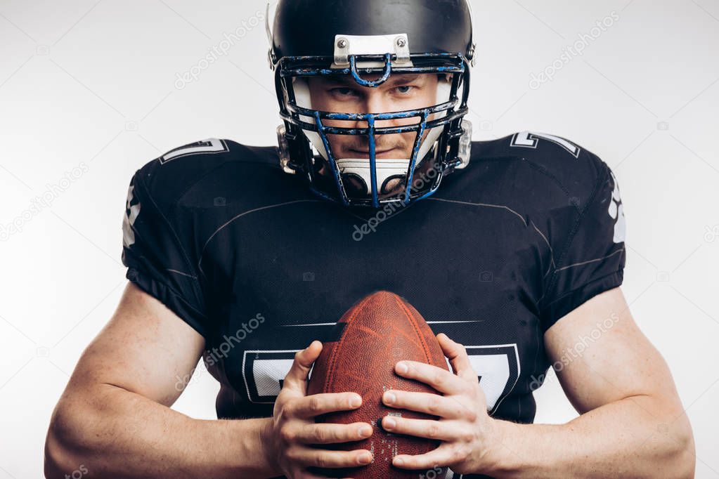 Muscular american football player in protective uniform and helmet holding ball