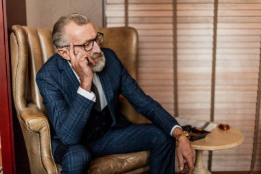 Resmi takım elbiseli yaşlı bir işadamı viski ve puro içiyor.