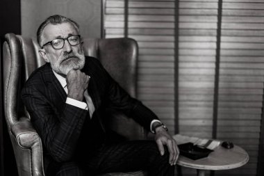 Resmi takım elbiseli yaşlı bir işadamı viski ve puro içiyor.