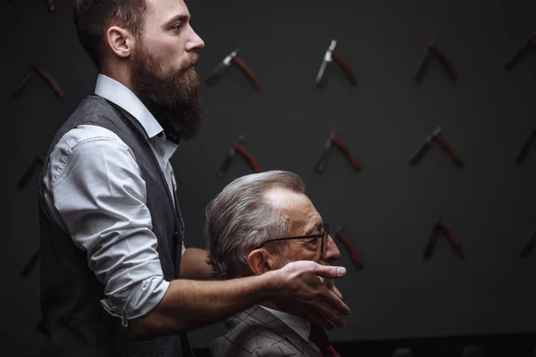 Barbudo viejo hombre de negocios sentado en la peluquería en silla de elegir el diseño de corte de pelo —  Fotos de Stock
