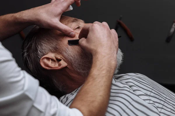 Viejo hombre consiguiendo su barba afeitado por barbero — Foto de Stock