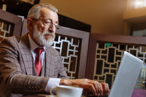 在他的办公室观念中，老商人在喝咖啡休息时间带着笔记本电脑 — 图库照片
