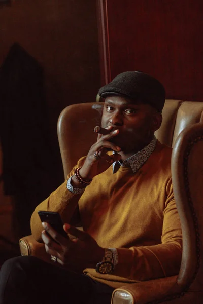 Hombre afroamericano vistiendo sombrero negro, en una silla, fumando ciga — Foto de Stock