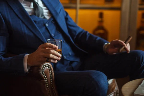 Karanlık arka planda bir bardak viski ve puro olan yaşlı bir işadamı. — Stok fotoğraf