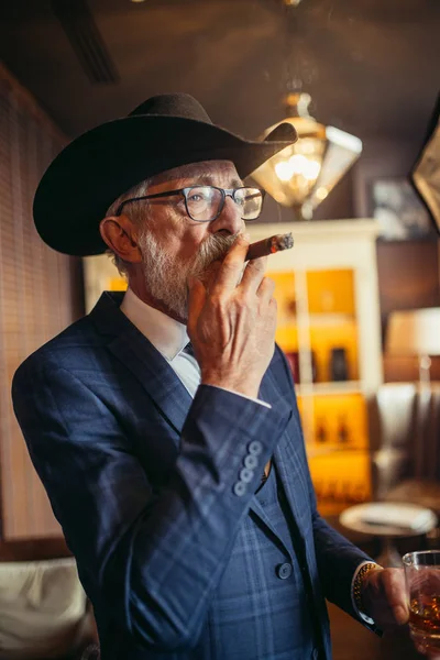 Retrato de anciano macho dandy en big hat fuma cigarro y bebe alcohol . — Foto de Stock