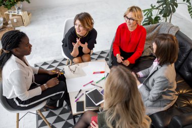 Çok ırklı kadın meslektaşlar masanın etrafında oturup grafik çiziyor.