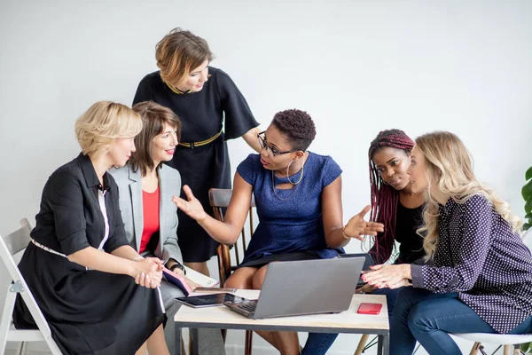 Позитивные женщины обсуждают план организации, сидя за столом с ноутбуком — стоковое фото