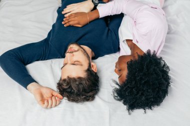 Genç çift yatak odasında birlikte uyuyor, birbirlerine tatlı tatlı sarılıyorlar.