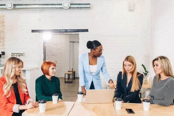 Afrikaanse vrouwelijke baas vertellen haar vrouwelijke werknemers, zit in witte zaal. — Stockfoto