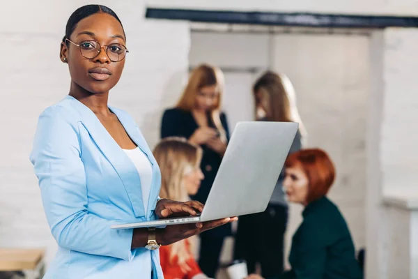 Affari nero donna regolazione computer portatile, in piedi con i colleghi di ufficio dietro — Foto Stock