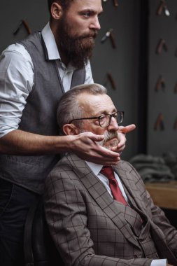 Sakallı yaşlı işadamı berber dükkanında oturuyor ve saç kesimini seçiyor.