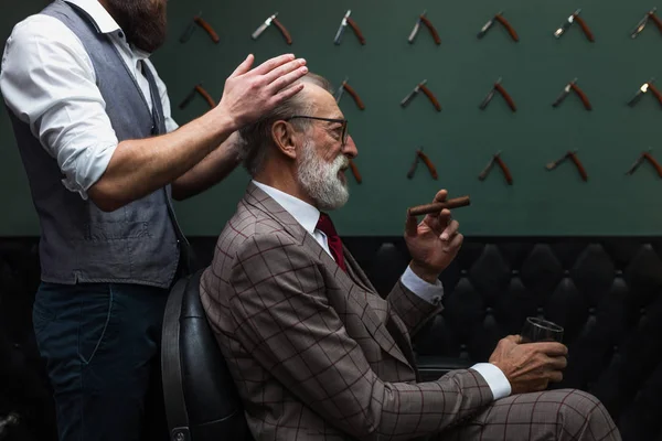 Homem de negócios velho barbudo sentado na barbearia na cadeira escolhendo design de corte de cabelo — Fotografia de Stock