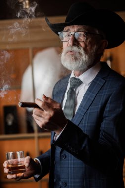 Geniş kenarlı şapkalı şık yaşlı adam ve zengin mavi adam elbisesi dumanı.