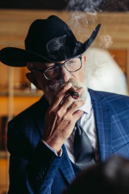 Geniş kenarlı şapkalı şık yaşlı adam ve zengin mavi adam elbisesi dumanı.