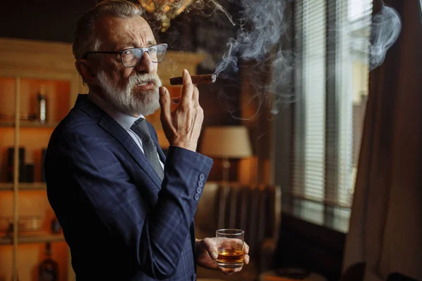 Anciano hombre de negocios en traje formal con whisky y cigarro en el interior de lujo — Foto de Stock