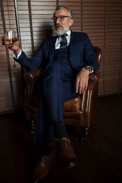Resmi takım elbiseli yaşlı işadamı, lüks bir yerde viski ve puro içiyor. — Stok fotoğraf