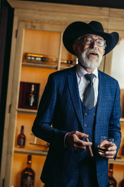 Büyük şapkalı yaşlı erkek züppenin portresi puro ve içki içiyor. — Stok fotoğraf