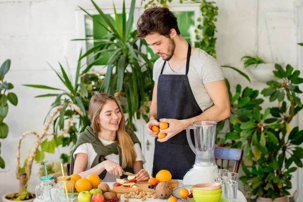 Stilig man med mandariner tittar flicka styckning frukter — Stockfoto