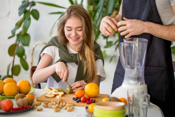 Positivo menina bonita sentada à mesa e cortando um quivi — Fotografia de Stock