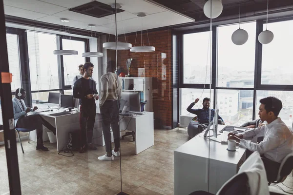 Hombres de negocios en un espacio abierto oficina interior con una ventana panorámica, tiro largo —  Fotos de Stock