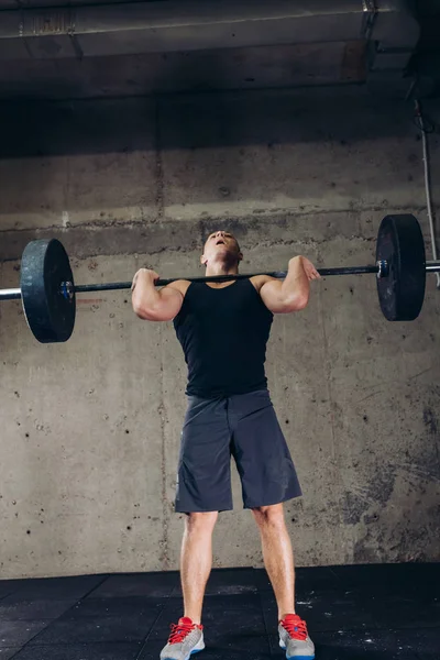 Chico deportivo haciendo ejercicio con barra de pesas en el gimnasio — Foto de Stock