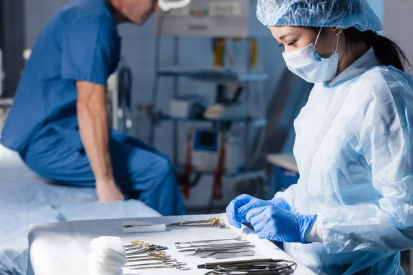 Herramientas quirúrgicas tumbadas en la mesa con la enfermera cerca y cirujanos en el fondo. — Foto de Stock