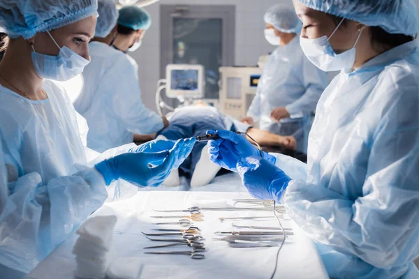 Herramientas quirúrgicas tumbadas en la mesa con la enfermera cerca y cirujanos en el fondo. — Foto de Stock