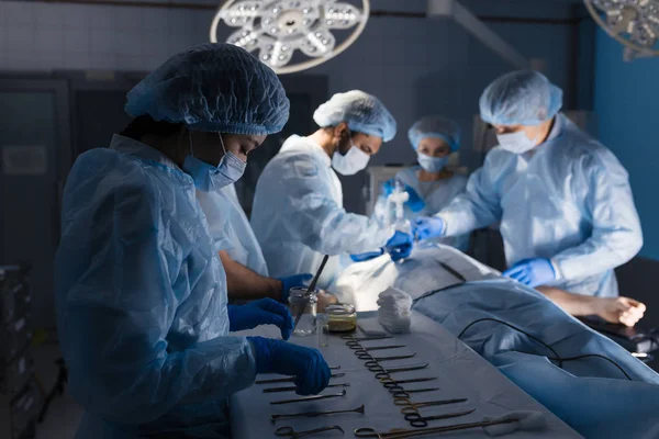 Narzędzia chirurgiczne leżące na stole z pielęgniarką w pobliżu i chirurgami w tle. — Zdjęcie stockowe