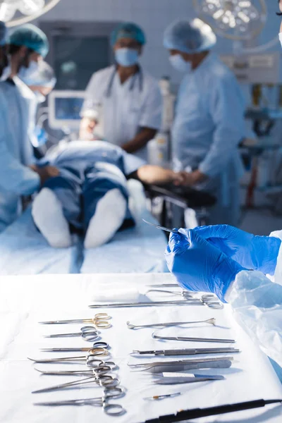 Ferramentas cirúrgicas deitado na mesa com a enfermeira perto e cirurgiões em segundo plano . — Fotografia de Stock