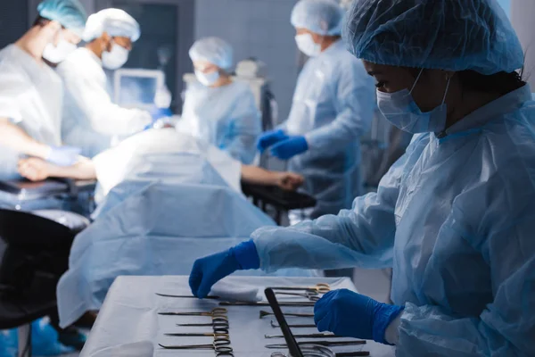 Narzędzia chirurgiczne leżące na stole z pielęgniarką w pobliżu i chirurgami w tle. — Zdjęcie stockowe