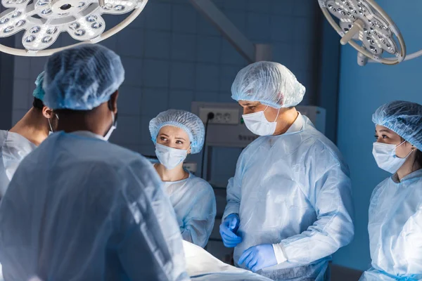 Equipo diverso de cirujanos, asistentes y enfermeras que realizan cirugía invasiva — Foto de Stock