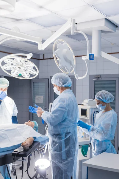 Assistant helping surgeon to put on latex gloves while standing in surgery — Stock Photo, Image