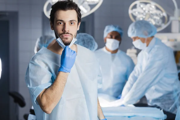 Kirurgen ser på kameran med kollegor — Stockfoto